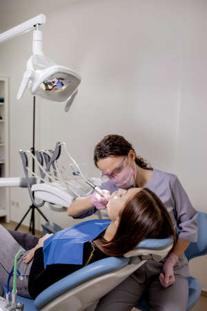 Adult woman visiting a dental office. Dentist hands in rubber protective gloves using white polishing stone for patient.の写真素材