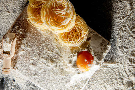 Freshly cooked pasta is lying on a dark surface dusted with flour. Italian pasta. Tagliatelle. Raw pasta. Italian pasta recipe. Top view, copy space.の写真素材