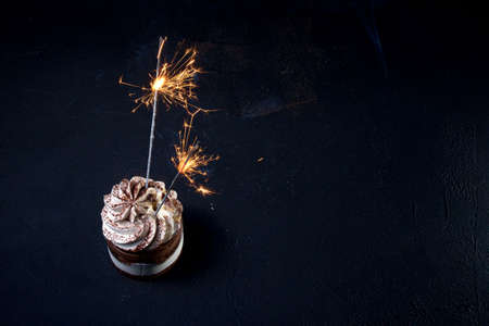 Delicious birthday cupcake with firework candle on table against dark backgroundの写真素材