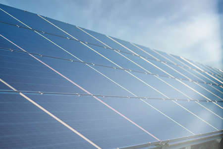 Solar Power Station in Green Field on Sunny day. Aerial view. Solar Panels Stands in a Row in Field for Power Production. Drone fly over Solar Farm. Renewable green energy. Alternative energy sourcesの写真素材