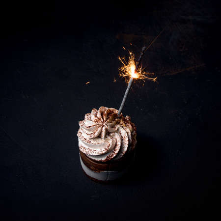 Delicious birthday cupcake with firework candle on table against dark backgroundの写真素材
