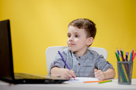 Happy Child using digital laptop doing homework on yellow background. Social Distancing, E-learning...