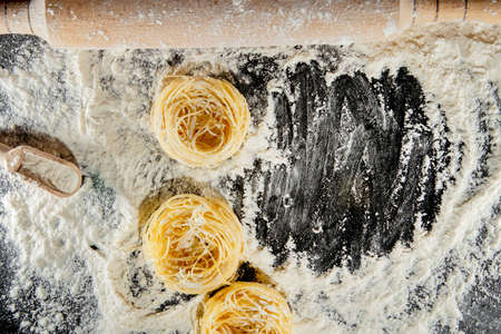 Freshly cooked pasta is lying on a dark surface dusted with flour. Italian pasta. Tagliatelle. Raw pasta. Italian pasta recipe. Top view, copy space.の写真素材