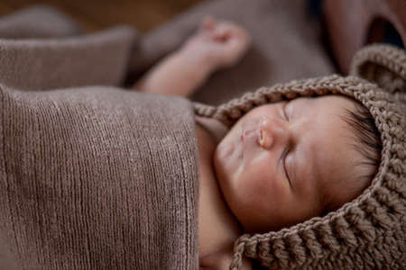 Newborn baby, beautiful infant lies in brown fur blanket on wood background, 10 days old girl sleeping in the bed. Copy space.の写真素材