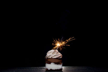 Delicious birthday cupcake with firework candle on table against dark backgroundの写真素材