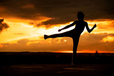 Silhouette of a fitness woman stretching at sunset with the sun in the background.の写真素材