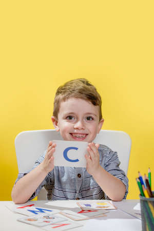 Happy smiling little preschool boy shows letters at home making homework at the morning before the school starts. English learning for kids.の写真素材