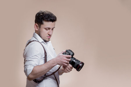 photographer with camera on brown background, successful professional male looks at photos on screen...