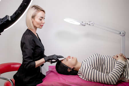 Cosmetologist, beautician making facial treatment with ultrasonic spatula to young woman, face skin scrubber treatment with ultrasonic spatula, facial cleansing procedure in beauty salon.の写真素材