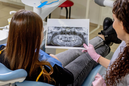 Dentist explaining the details of a x-ray teeth picture to his patient in clinic. Oral care,...