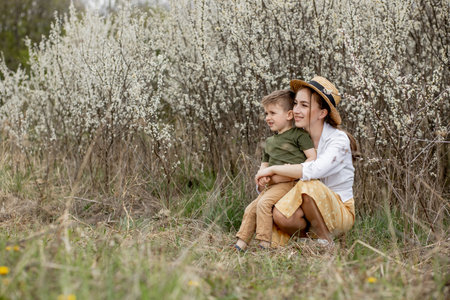 Happy mother and son having fun together. Mother gently hugs her son. In the background white flowers bloom. Mother's day.の写真素材