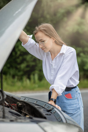 Young woman standing near broken down car with popped up hood having trouble with her vehicle.