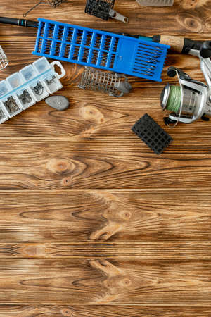 flat lay with fishing tackle, fishing rod and plastic box with fishing tackle and hooks, feeders on wooden planks, copy spaceの写真素材