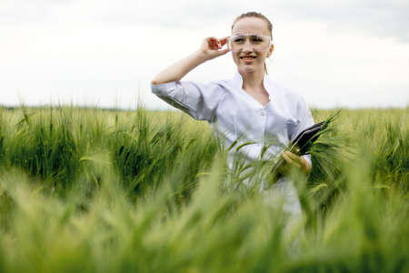 Young woman farmer wearing white bathrobe is checking harvest progress on a tablet at the green wheat field. New crop of wheat is growing. Agricultural and farm conceptの写真素材