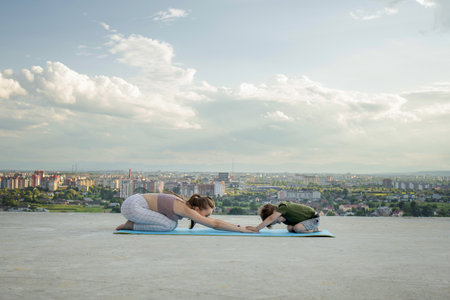 Mother and son doing exercise on the balcony in the background of a city during sunrise or sunset, concept of a healthy lifestyle.の写真素材