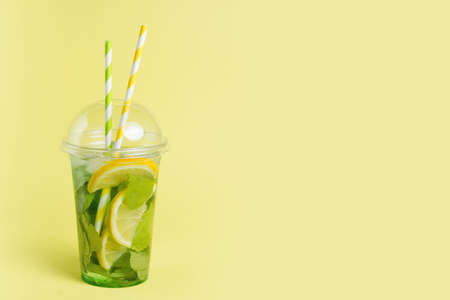 Mojito cocktail in a plastic glass with a tube on a yellow background. ool drink in the summer for takeaway. Place for text.の写真素材