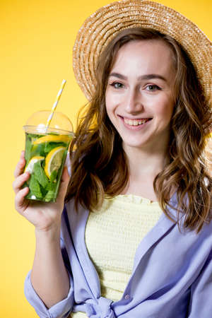 Beautiful young woman with plastic cup of fresh cocktail on yellow backgroundの写真素材