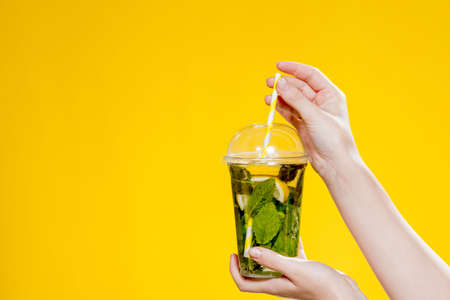 Mojito cocktail in a plastic glass with a tube on a yellow background. ool drink in the summer for takeaway. Place for text.の写真素材