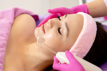 Darsonvalization of the face or rejuvenation of the face with the help of electrotherapy. Photo of darsonval for the face. Current therapy. The patient is at the beauticianの写真素材