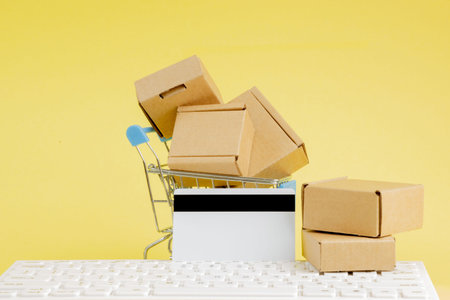 Online shopping concept. Shopping cart with small boxes inside on yellow background. Logistics and...