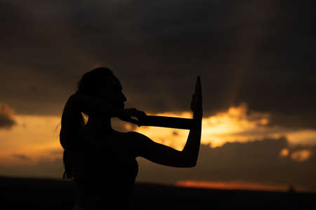 Silhouette of a fitness woman stretching at sunset with the sun in the background.の写真素材