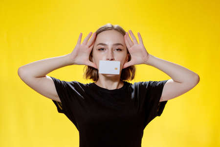 Smiling young woman holding credit card on yellow backgroundの写真素材