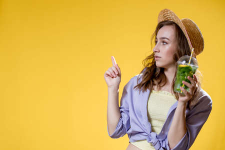 Beautiful young woman with plastic cup of fresh cocktail on yellow backgroundの写真素材