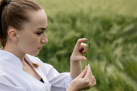 Scientist in a white coat looking at green plants in the field.の写真素材