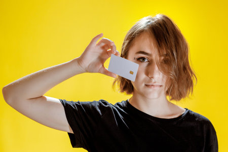 Smiling young woman holding credit card on yellow background