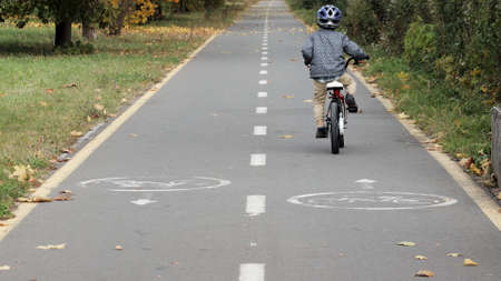 Little boy in a helmet on a bicycle rides on a bike path in the parkの写真素材