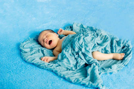 Newborn 14 day old baby boy lying on his back crying on blue wrap cloth.の写真素材