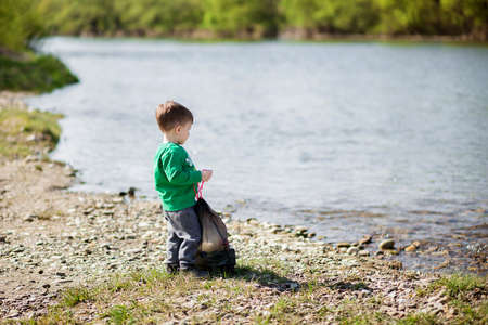 Little boy collecting garbage and plastic bottles on the beach to dumped into the trash. Save environment concept.の写真素材
