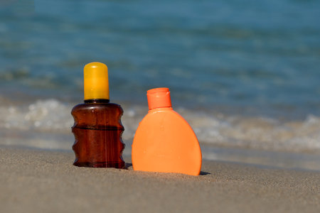 Closeup of sunscreen protection set on sandy beach at tropical seaside on warm sunny day. Skin care...