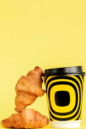 Paper cup of coffee and croissants on a yellow background, Copy space.の写真素材
