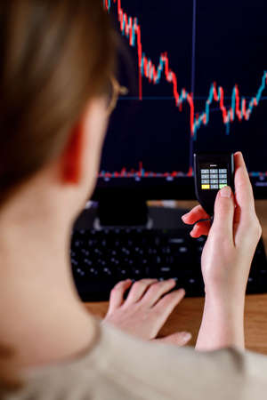 Woman trader investor analyst enter the password on cryptocurrence hardware cold wallet on stock market graph background. Secure cryptocurrency storage.の写真素材