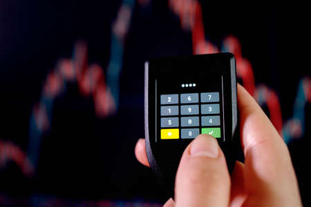 Close up hand enter the password on cryptocurrence hardware cold wallet on stock market graph background. Secure cryptocurrency storage.の写真素材