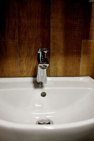 Bathroom interior with white sink and faucet. Water faucet and white sink and ceramic tile with imitation brown wood.の写真素材