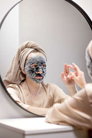 Young woman applying face mask in bathroom and smiling. Beautiful woman in front of a mirror doing beauty treatmentsの写真素材