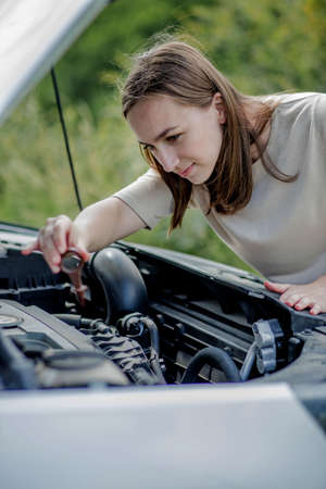 The woman pulls out a probe in her car engine to check the oil level. The woman manages the car herself.の写真素材