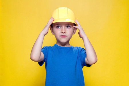 Portrait preschooler in a helmet builder on yellow background.