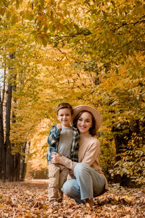 Portrait of Mother and son walking outdoors on a sunny autumn day. The family is dressed in autumn clothes. happy together.の写真素材