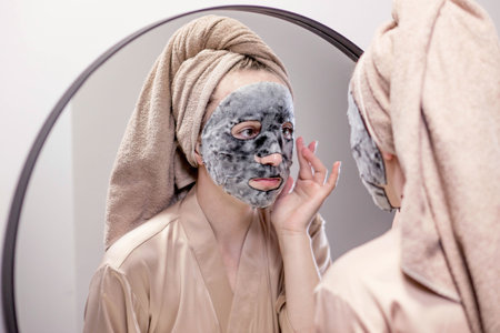 Young woman applying face mask in bathroom and smiling. Beautiful woman in front of a mirror doing beauty treatmentsの写真素材