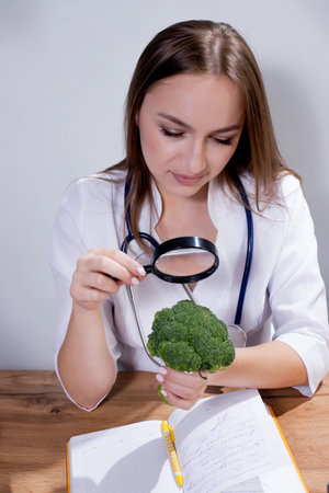 A female nutritionist looks through a magnifying glass at broccoli in her office. Healthy eating.の写真素材