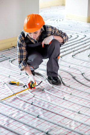 A female construction worker checks the installation of a warm floor with a tape measure at the construction siteの写真素材