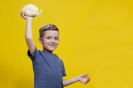 Cauliflower in the hands of a cheerful boy on a yellow background. Health food.の写真素材