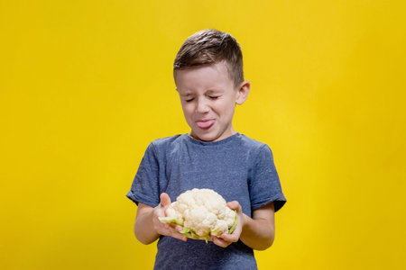 A charming little boy refusing to eat cauliflower. Health food.の写真素材