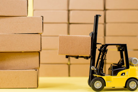 Forklift truck raises cardboard boxes on a yellow background. Cargo sorting concept.の写真素材