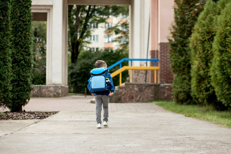 Little first grader with a blue backpack goes to school.の写真素材