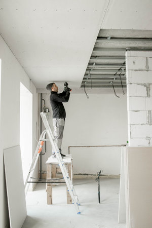 The worker attaches plasterboard on metal frame. Installation of ceiling.の写真素材