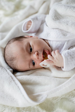 Newborn baby lying with baby pacifier covered with white blanket